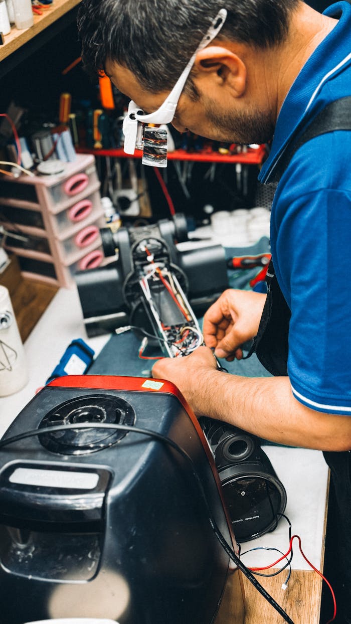 A technician carefully repairs a vacuum cleaner in a cluttered workshop, showcasing skilled craftsmanship.