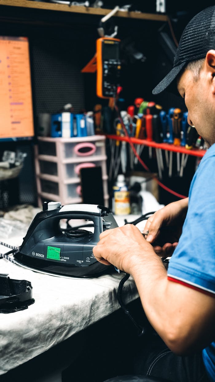 Technician in workshop repairing an electric iron with tools and equipment in the background.